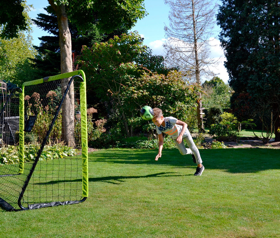 Junge köpft einen Fußball vor einem EXIT Fußballtor »Tempo 3000«.