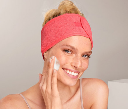 Frau schäumt ihr Gesicht ein und trägt ein korallfarbenes Kosmetik-Stirnband (2 Stück).