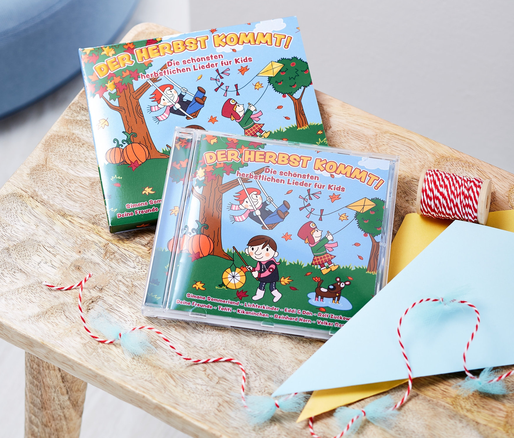 Zwei CDs mit Kinderliedern auf einem Holzhocker zusammen mit einem Kinder-Drachenbau-Set.