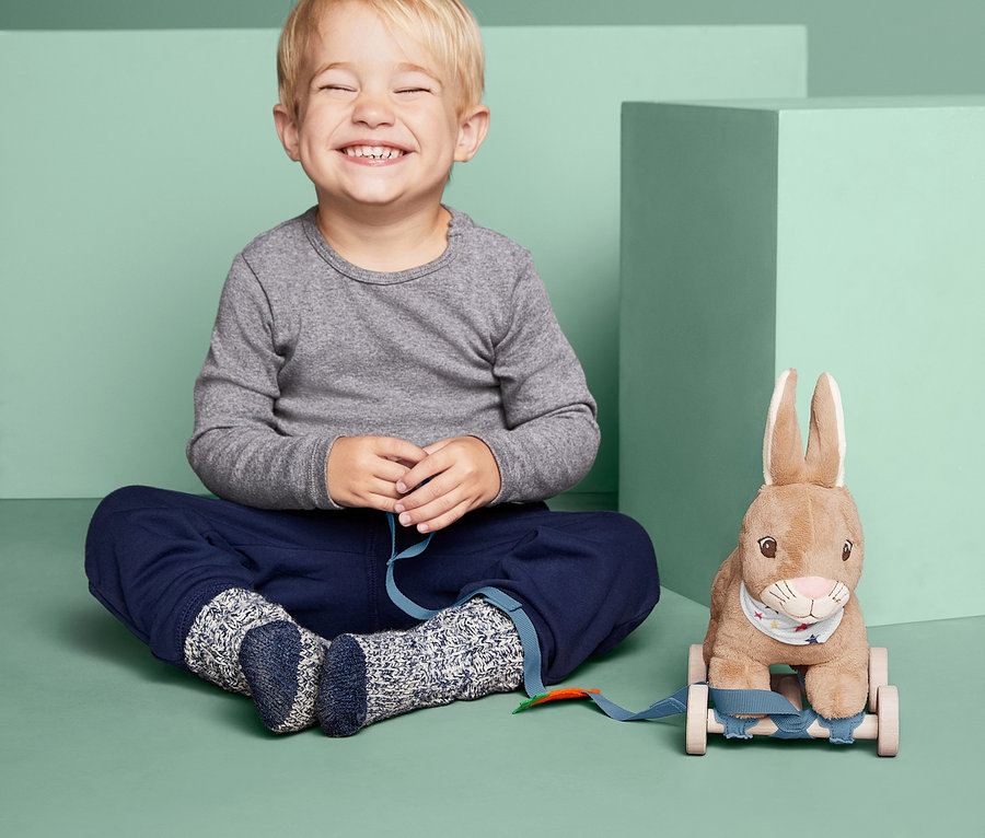 Ein Junge sitzt mit geschlossenen Augen neben dem Nachziehtier »Hoppel-Hase«.
