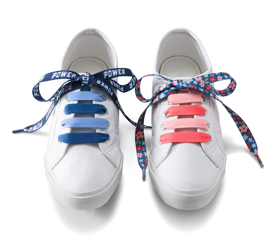 Zwei weiße Schuhe mit Kinder-Schnürsenkel mit Motiv, einmal blau und einmal mit Blumenmuster.