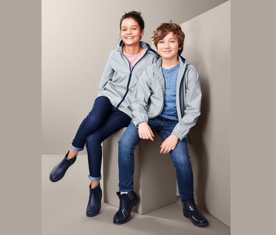 Kinder sitzen in reflektierenden Übergangsjacken und dunkelblauen Schuhen.