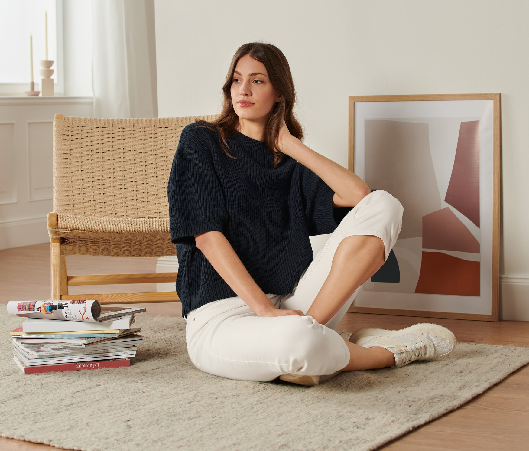 Frau sitzt auf einem Teppich und trägt einen Grobstrick-Pullover.