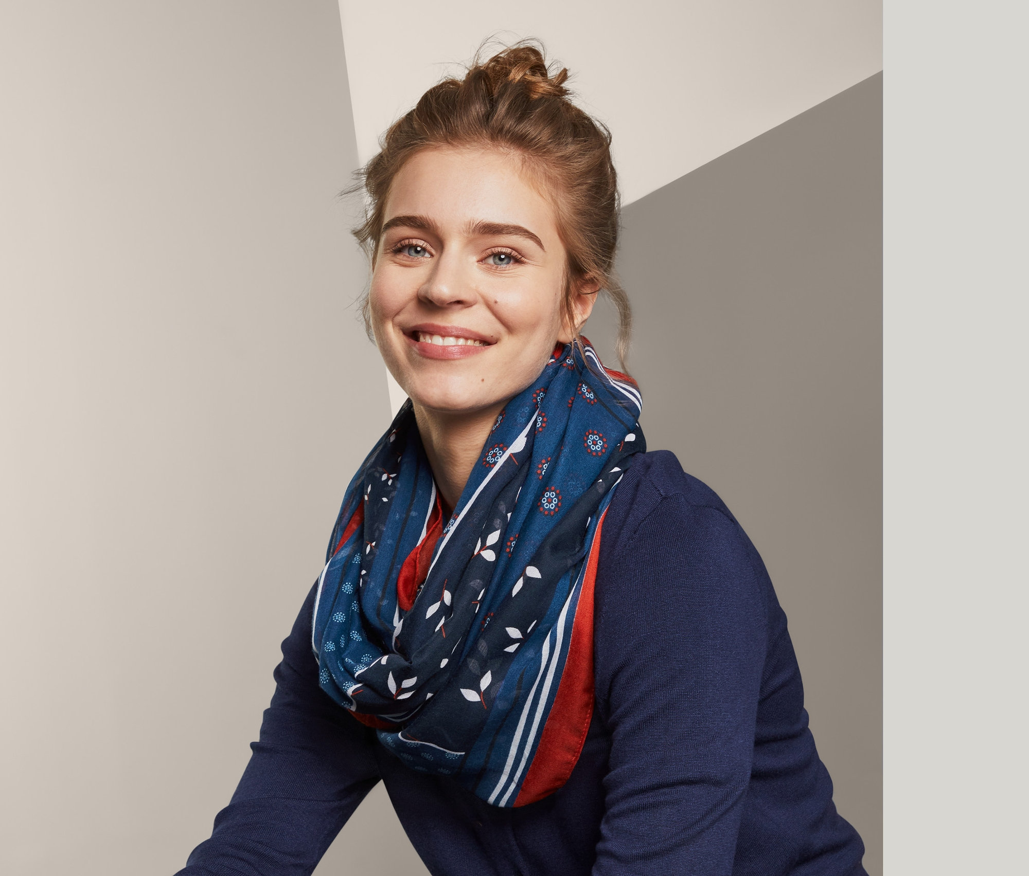 Lächelnde Frau sitzt und trägt einen Loop-Schal.