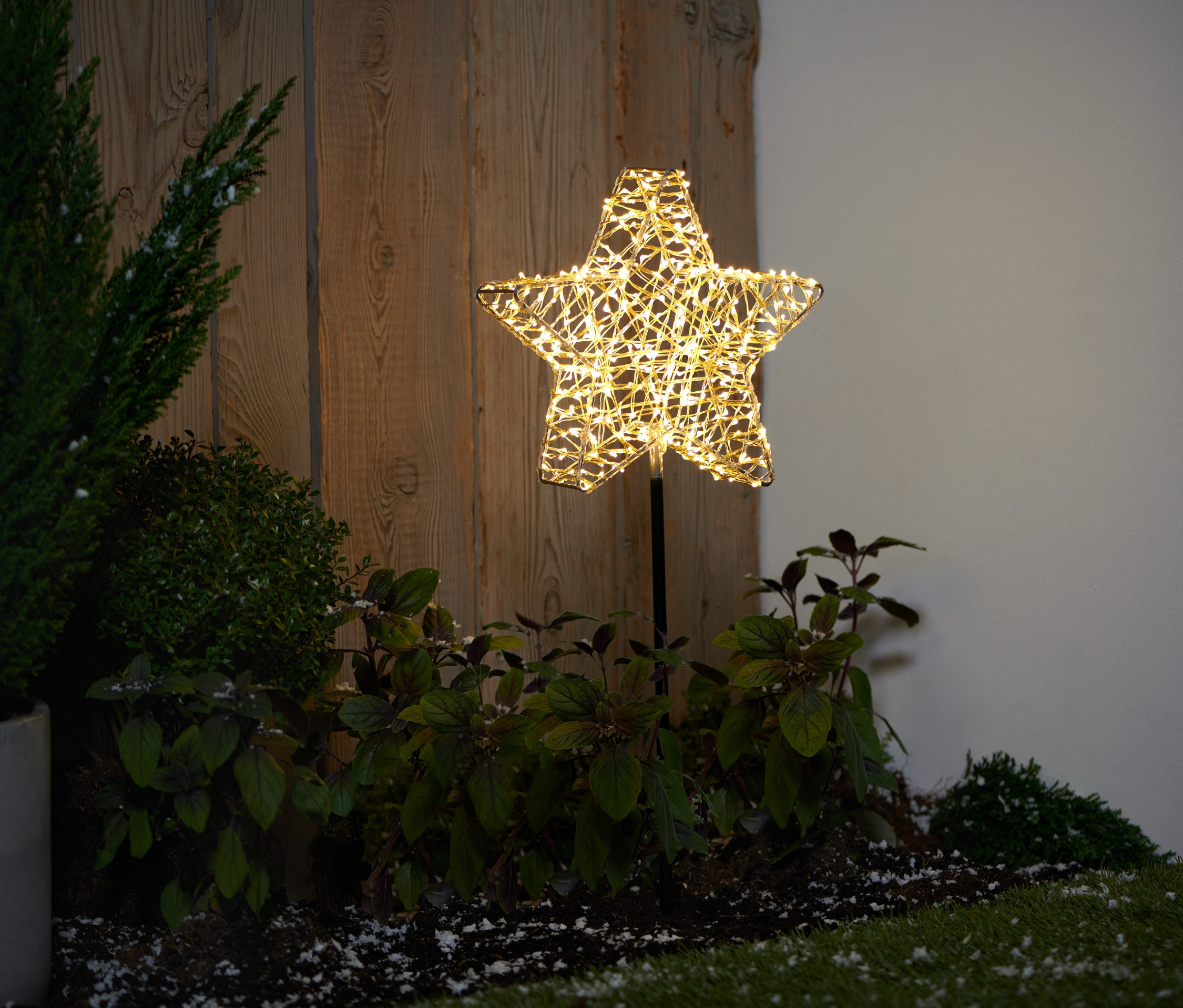 Ein 3D-LED-Outdoorstern mit Spieß steht auf einer Wiese neben Pflanzen.