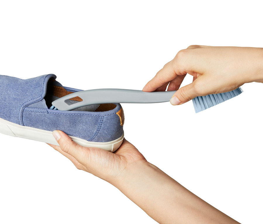 Hände reinigen einen blauen Stoffschuh mit einer 2-in-1-Grobschmutz-Schuhreinigungsbürste.