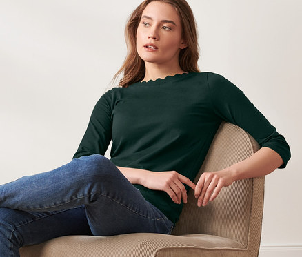 Frau sitzt im Sessel und trägt ein dunkelgrünes Shirt mit 3/4-Arm.