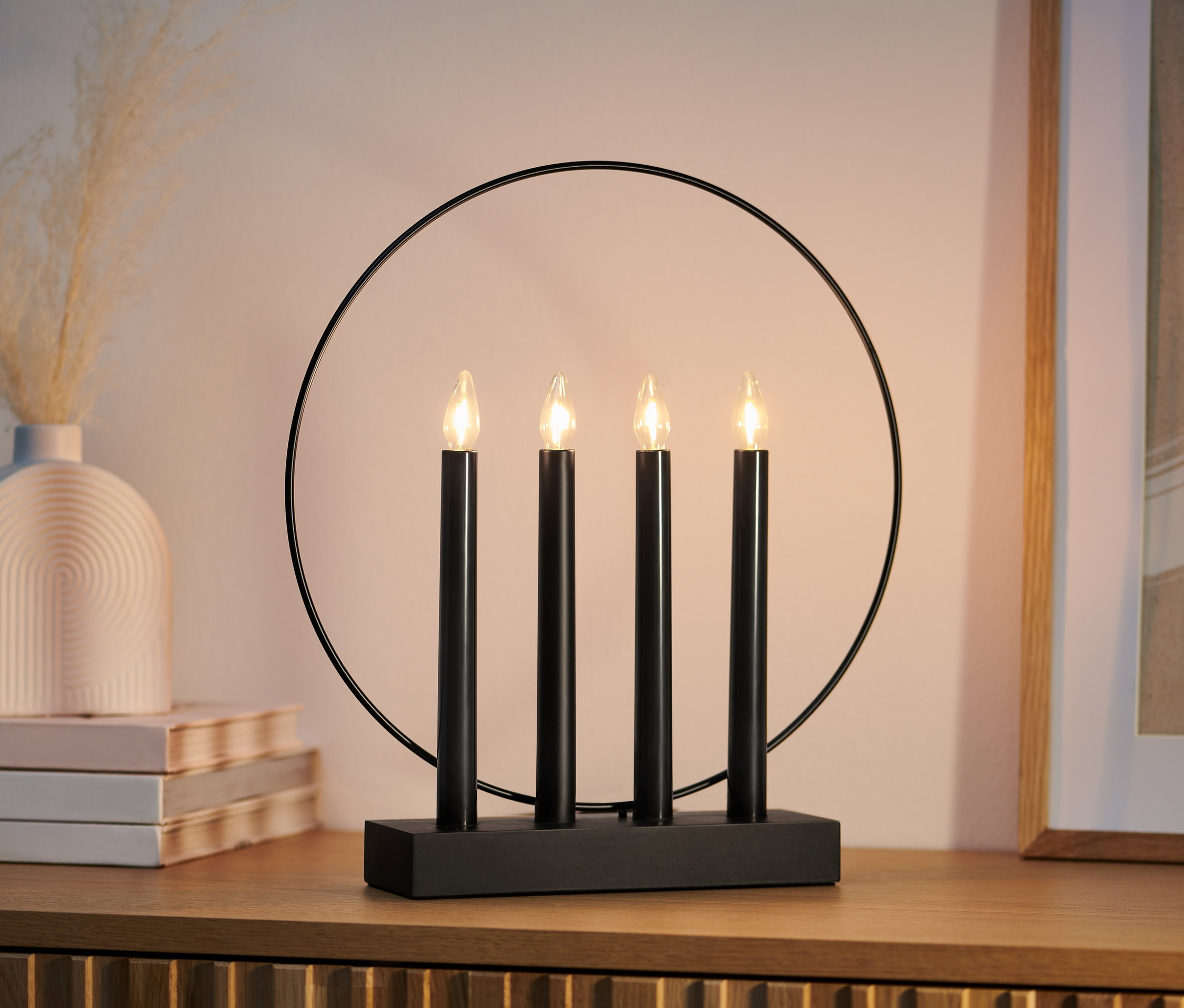 Vier schwarze LED-Kerzenleuchter »Ring« stehen auf einer Holzkommode.