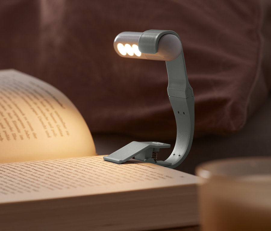 LED-Leselicht mit Akku ist an einem Buch auf einem Nachttisch befestigt.