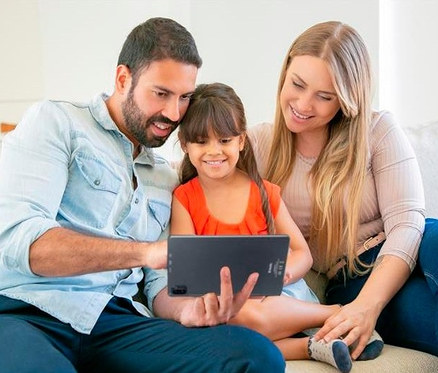 Eine Familie sitzt auf der Couch und schaut auf ein Tablet. Der Mann hält ein Readly Reader Android 12 Tablet mit Deutschlands größtem digitalem Kiosk.