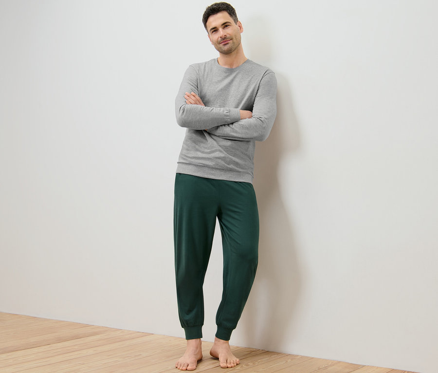 Mann posiert mit verschränkten Armen und trägt einen grauen Pyjama und eine grüne Pyjamahose.