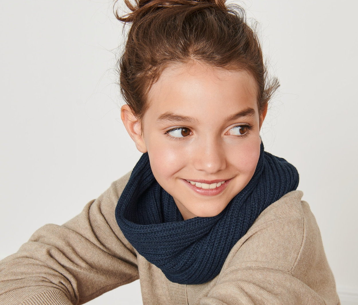 Lächelndes junges Mädchen sitzt mit dem Rücken zur Kamera und trägt einen Strickloop.