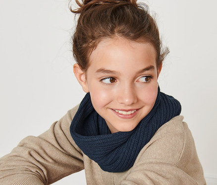 Lächelndes junges Mädchen sitzt mit dem Rücken zur Kamera und trägt einen Strickloop.