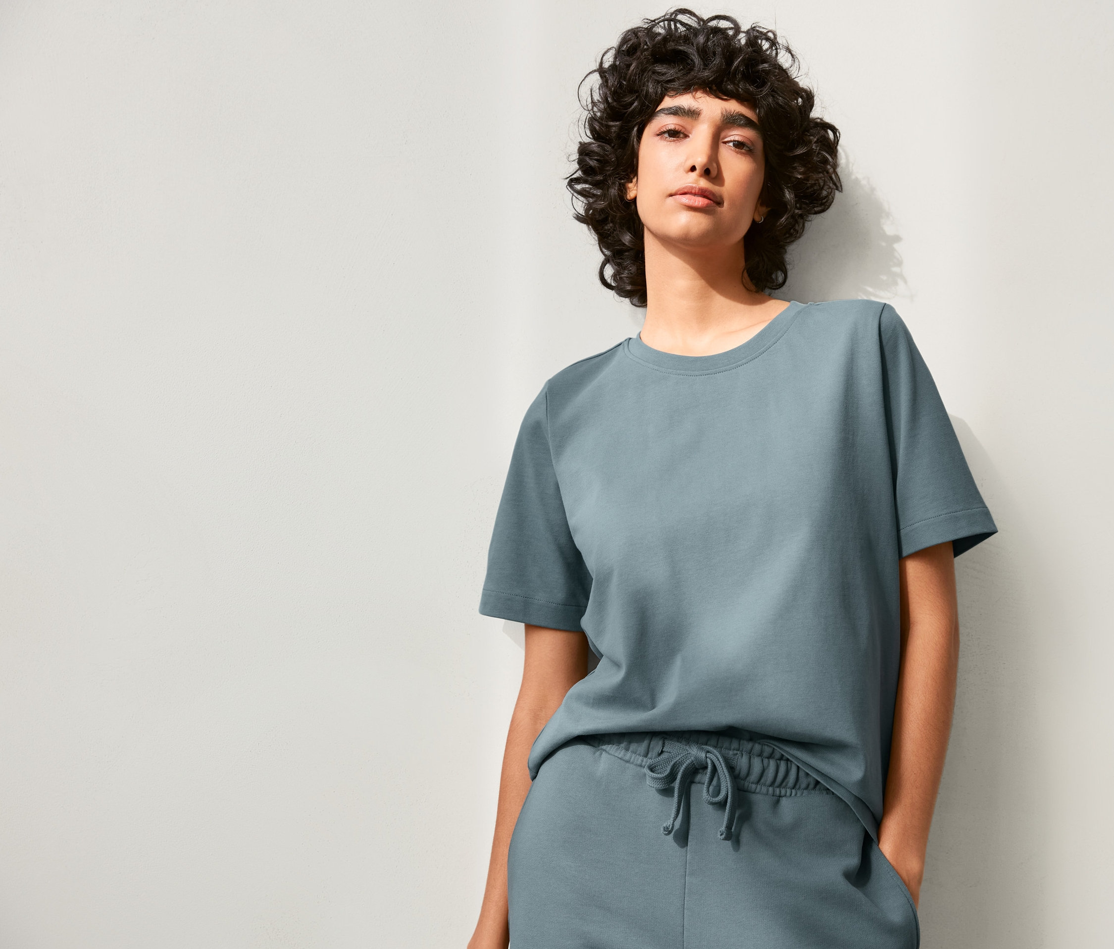 Frau posiert in stone blue NAH/STUDIO Heavy Weight Shirt und Trainingshose.