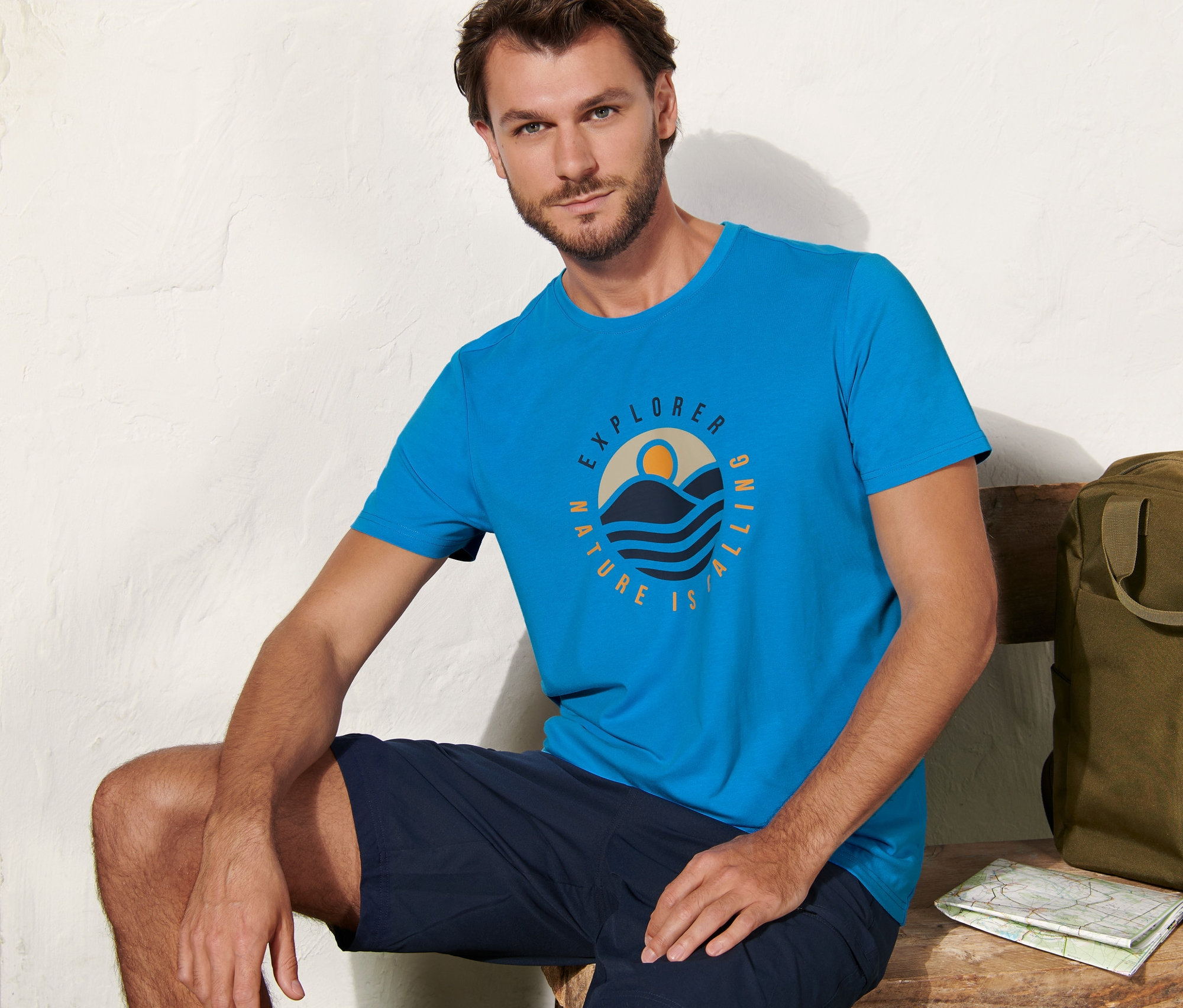 Mann sitzt auf Bank, trägt blaues T-Shirt mit Print.