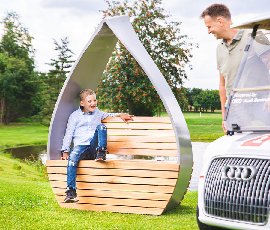 Ein Junge sitzt auf der Wings for Living Sitzbank »San Francisco Twin«, während ein Mann neben einem Golfwagen steht.