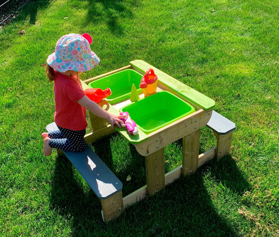 Mädchen sitzt auf einer Bank am Wendi Picknick- und Matschtisch und spielt mit Spielzeug.