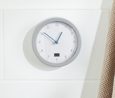 Eine Badwanduhr hängt an einer Wand neben einer Holzleiter mit einem beige-farbenen Handtuch.