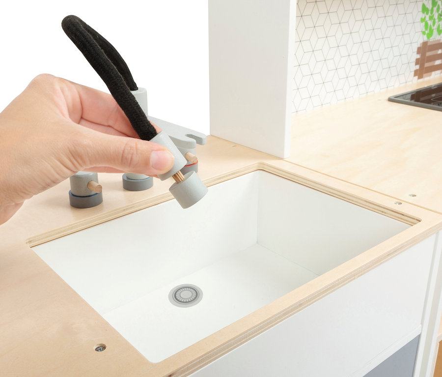 Eine Hand hält einen Wasserhahn über ein Spülbecken in einer small foot Kinderküche modular XL.