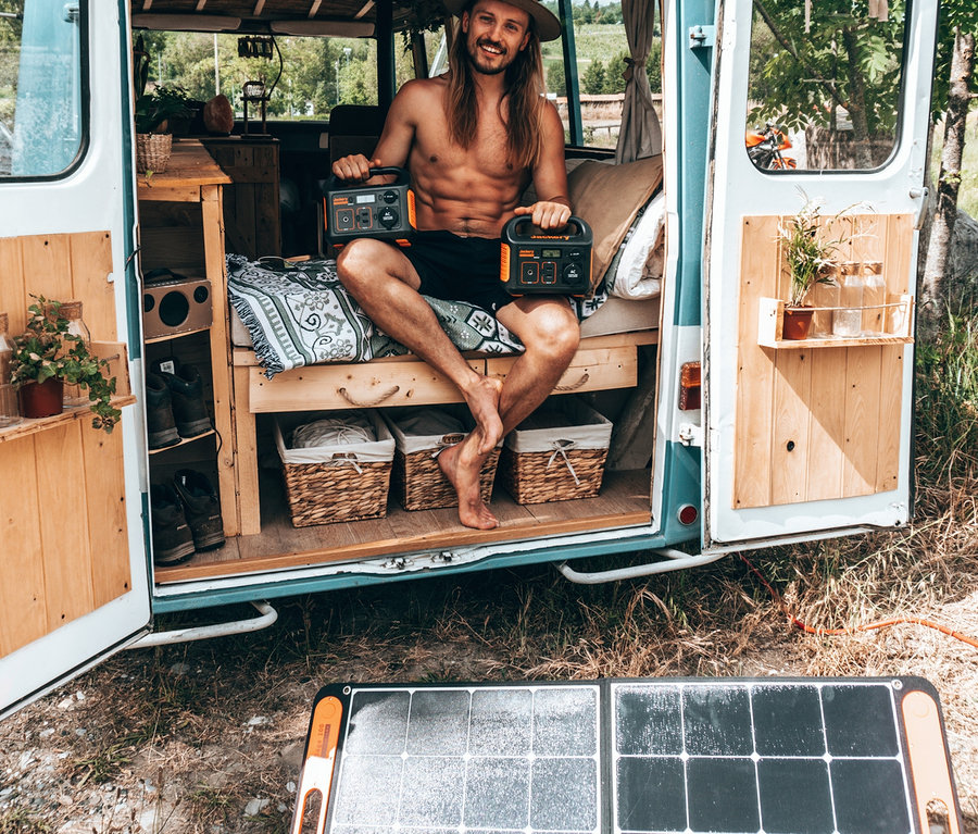 Mann sitzt in Van und hält zwei Jackery Explorer 240. Solarpanel SolarSaga 100 ist draußen.