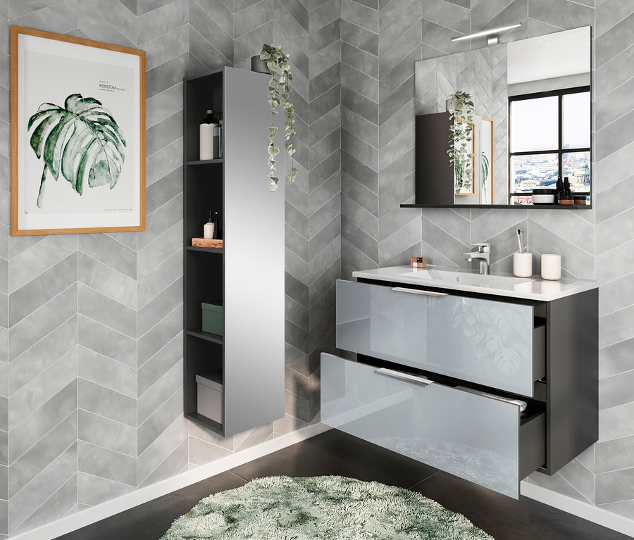 Das Badezimmer mit grauen Chevron-Wänden verfügt über ein Waschbecken mit zwei Schubladen, einen Spiegel und ein Wandregal sowie ein schmales, schwarzes Regal "Vasio" und einen Teppich aus Kunstfell.