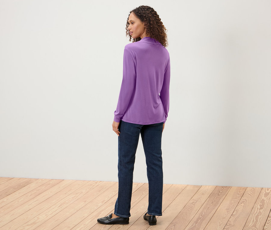 Frau blickt über die Schulter und trägt ein Blusenshirt mit V-Ausschnitt, Jeans und Slipper.