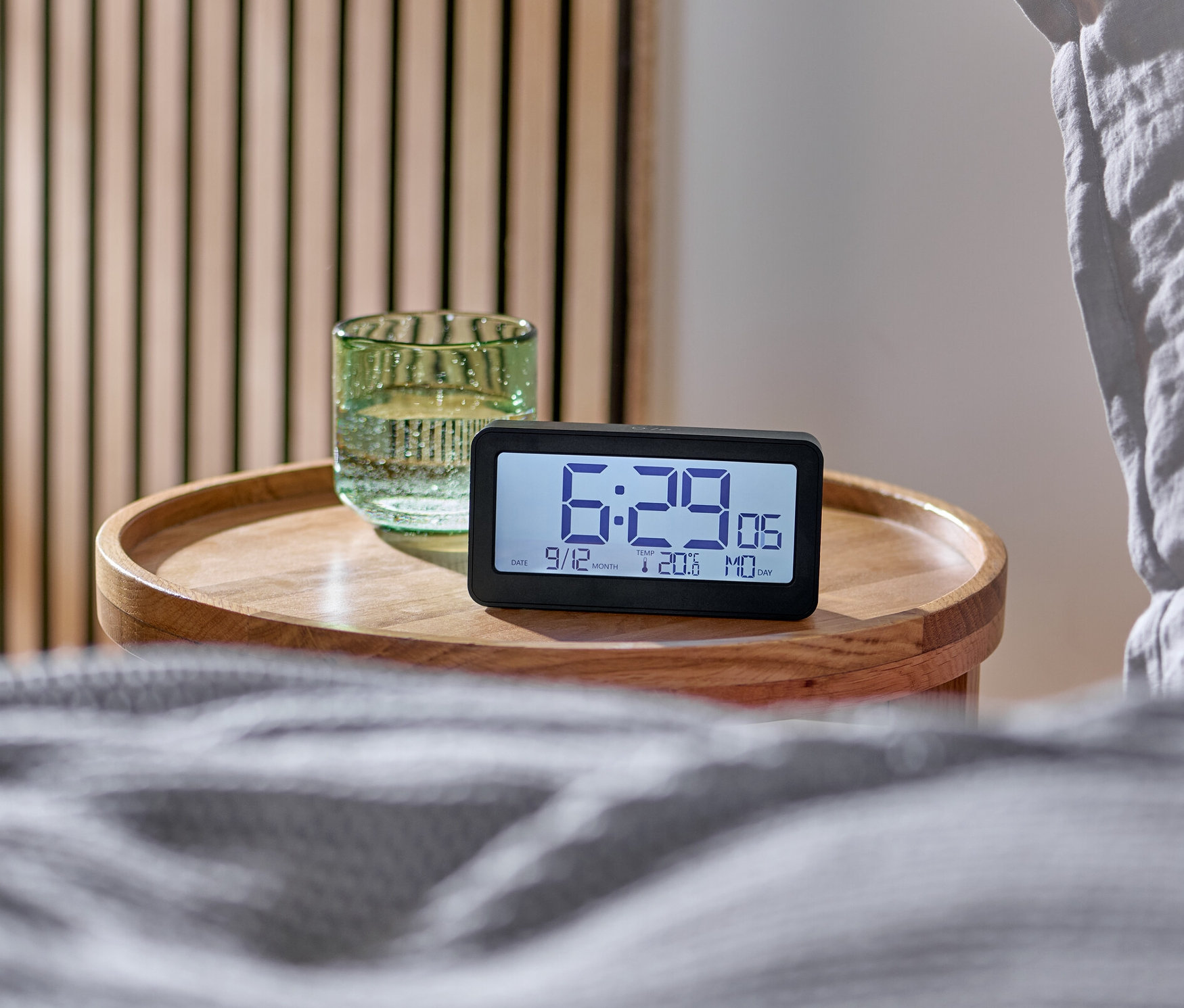 Digitaler LCD-Funkwecker auf einem Nachttisch neben einem Bett.