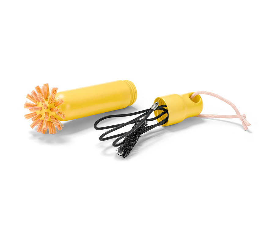 Eine gelbe 2-in-1-Abflussbürste mit orangefarbenen Borsten liegt neben einem Gehäuse mit schwarzen Reinigungsbürsten.