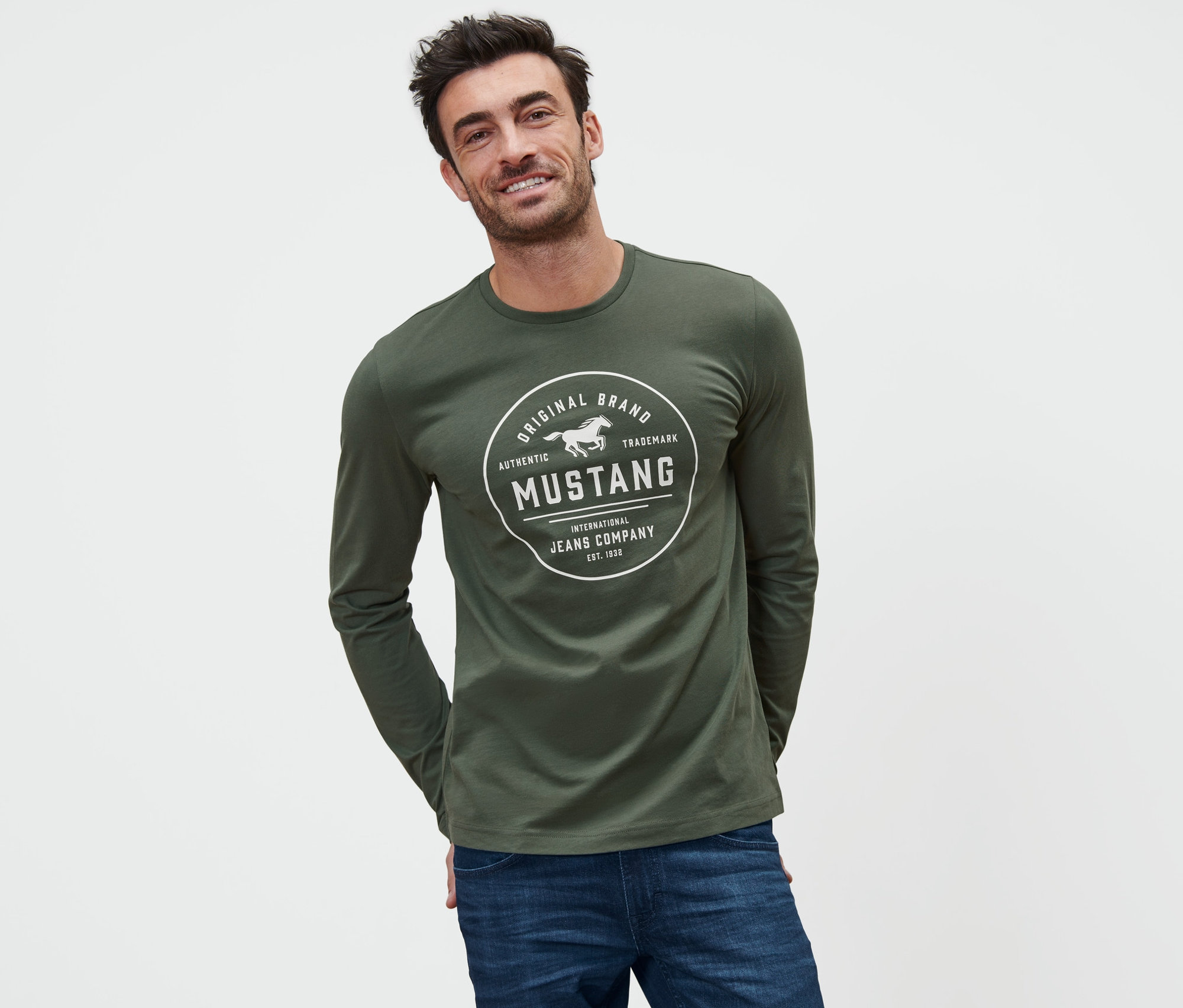 Ein lächelnder Mann trägt ein olivgrünes Longsleeve »Mustang« und blaue Jeans.