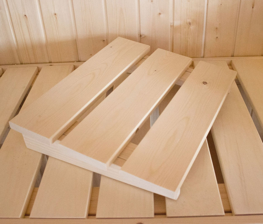 Eine hölzerne Kopfstütze aus dem Karibu Sauna-Zubehör-Set »Premium« liegt auf einer Holzbank in einer Sauna.