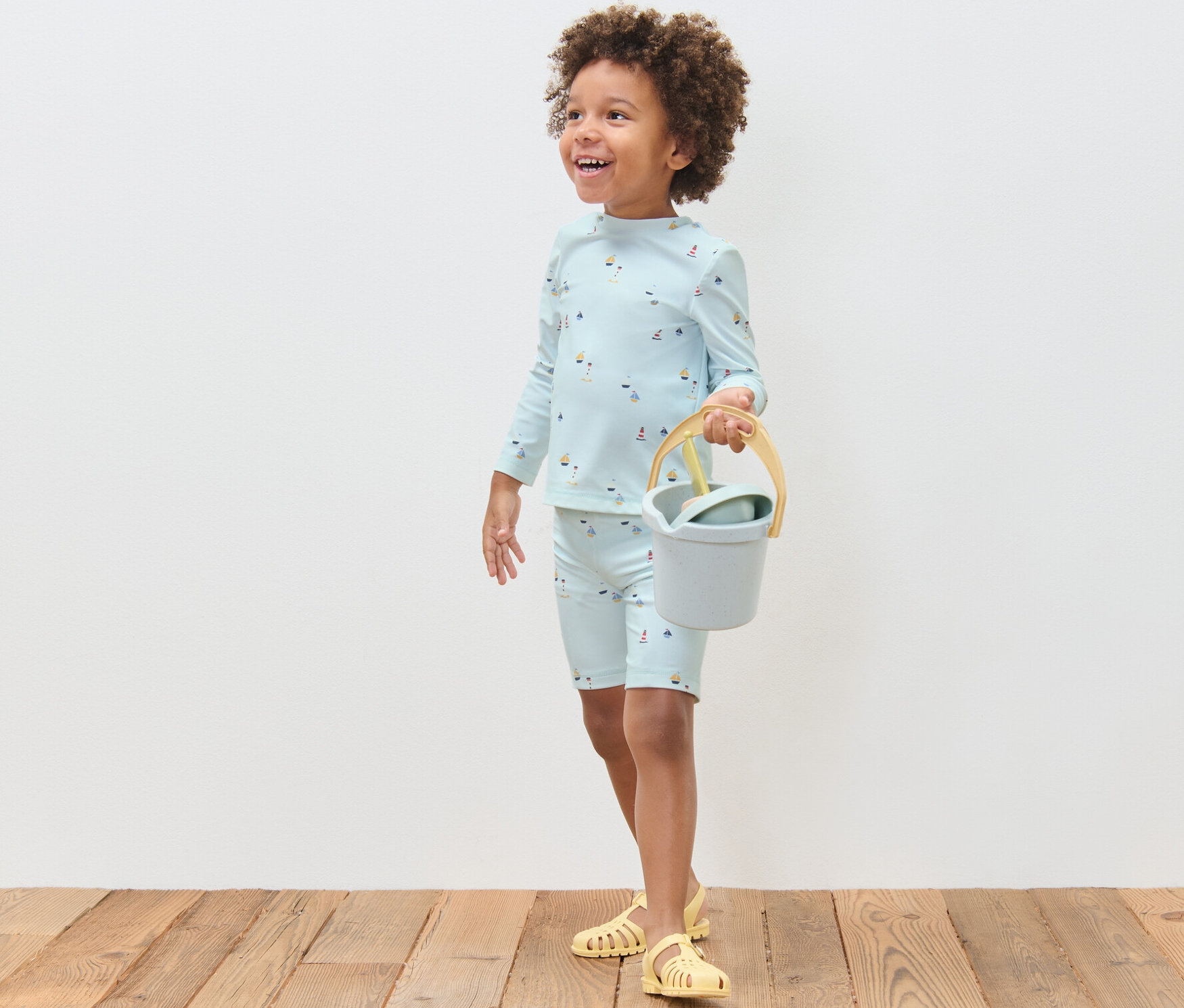 Junge trägt Kinder-Kombi mit UV-Schutzfaktor 80, maritim, und hält Eimer und Schaufel.