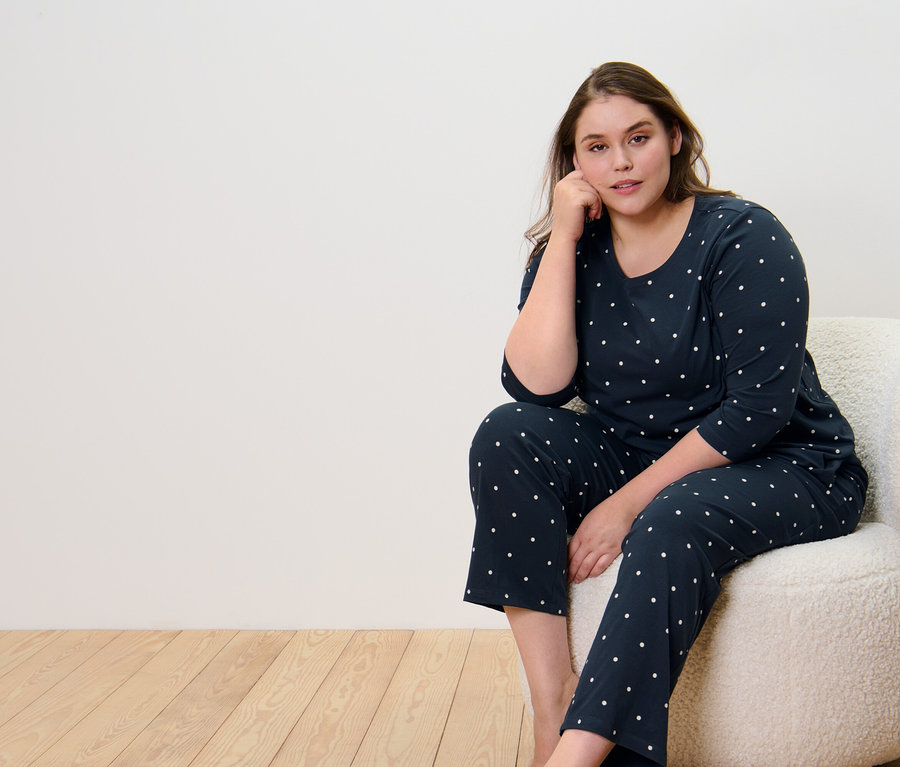 Frau sitzt auf Sessel und trägt Pyjama, Punkte.