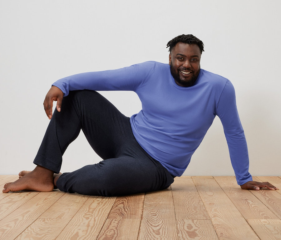 Mann sitzt auf einem Holzboden in einem blau-dunkelblauen Pyjama.
