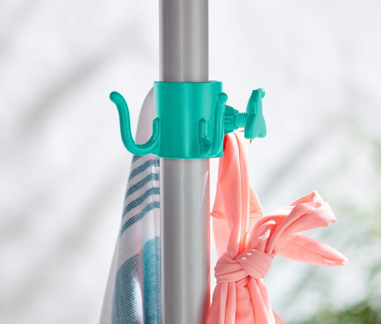 Zwei Sonnenschirm-Haken sind an einer silbernen Stange befestigt, an denen ein Handtuch und rosa Kleidung hängen.