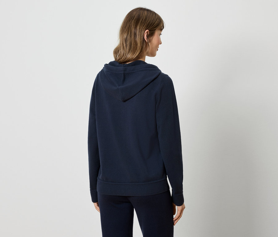 Frau mit dem Rücken zur Kamera trägt einen dunkelblauen Kapuzenpullover und eine Trainingshose.