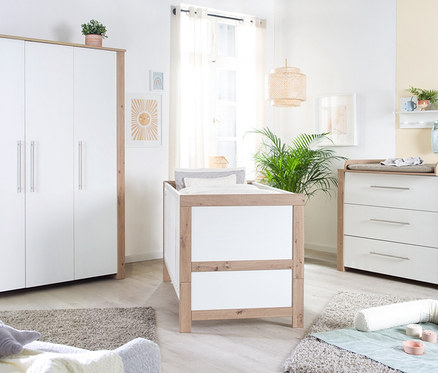 Ein Zimmer mit weißen Kindermöbeln mit Holzdetails, darunter ein roba Kombi-Kinderbett »Malo«, 70 x 140 cm, eine Kommode und ein Schrank.