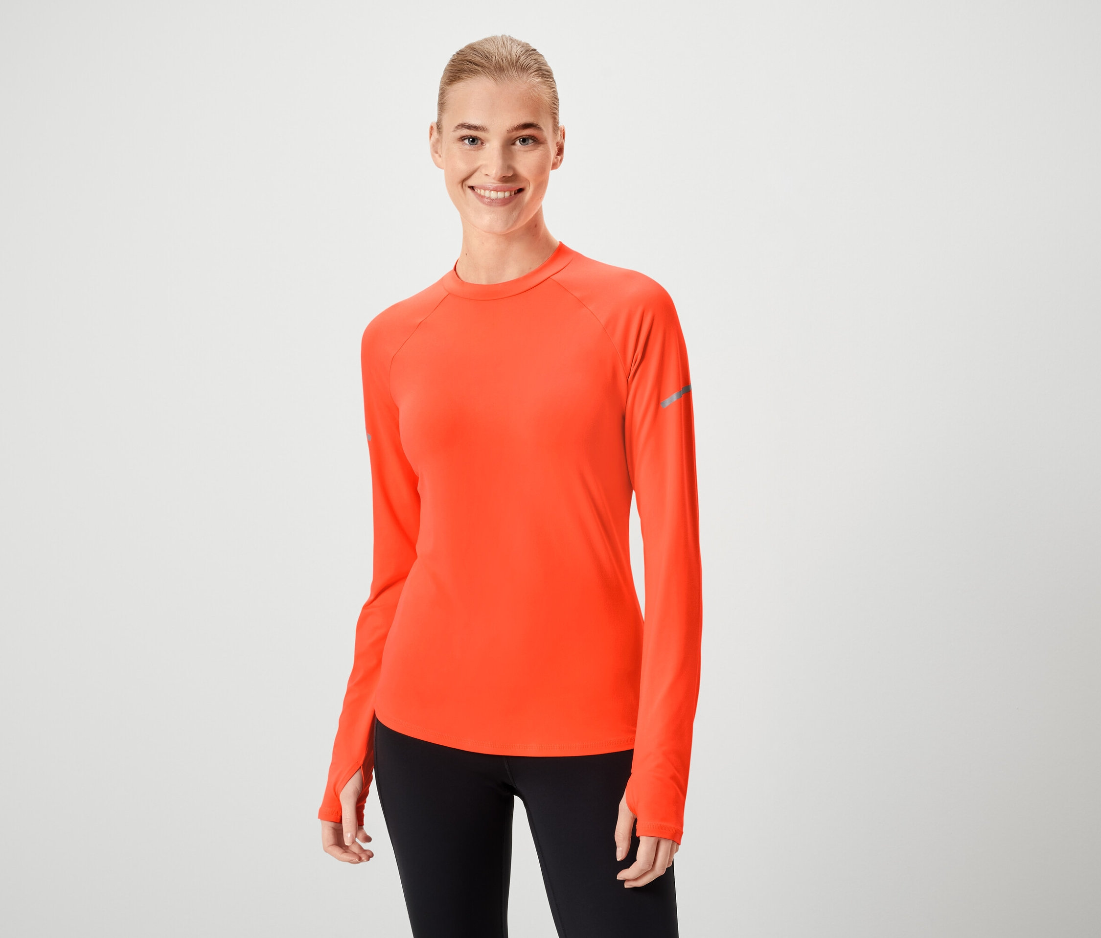 Eine Frau lächelt und trägt ein orangefarbenes Langarmshirt und schwarze Leggings.