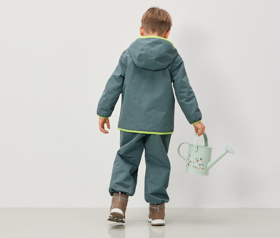 Junge in Kapuzenjacke und -hose hält eine Gießkanne.