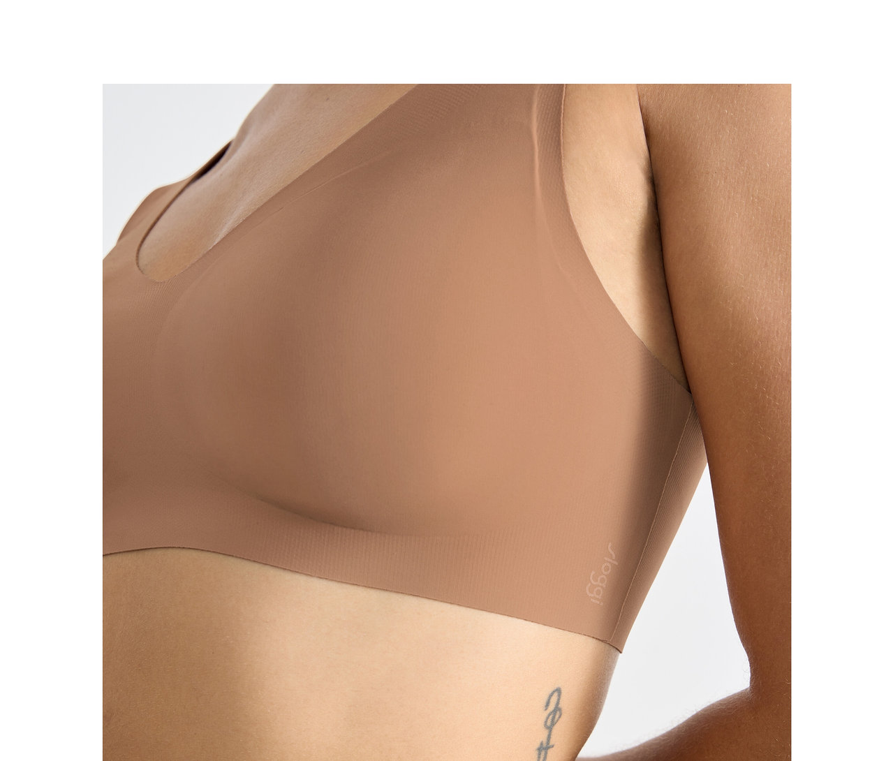 Nahaufnahme einer Person, die einen sloggi ZERO Feel 2.0 Bralette in Nostalgic Brown trägt, mit einem Tattoo an der Seite.