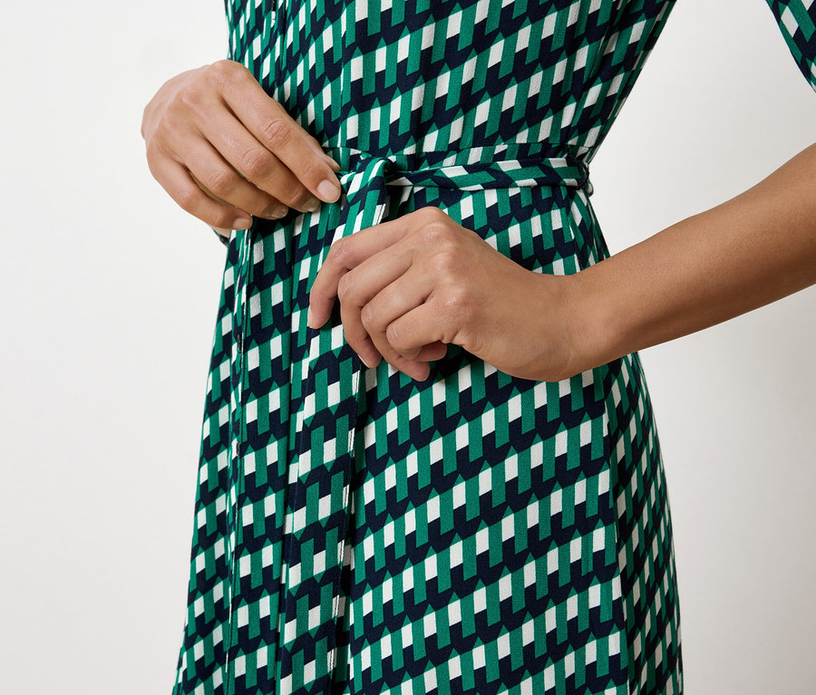 Frau bindet den Gürtel an einem grün-weiss-dunkelblauen Kleid.