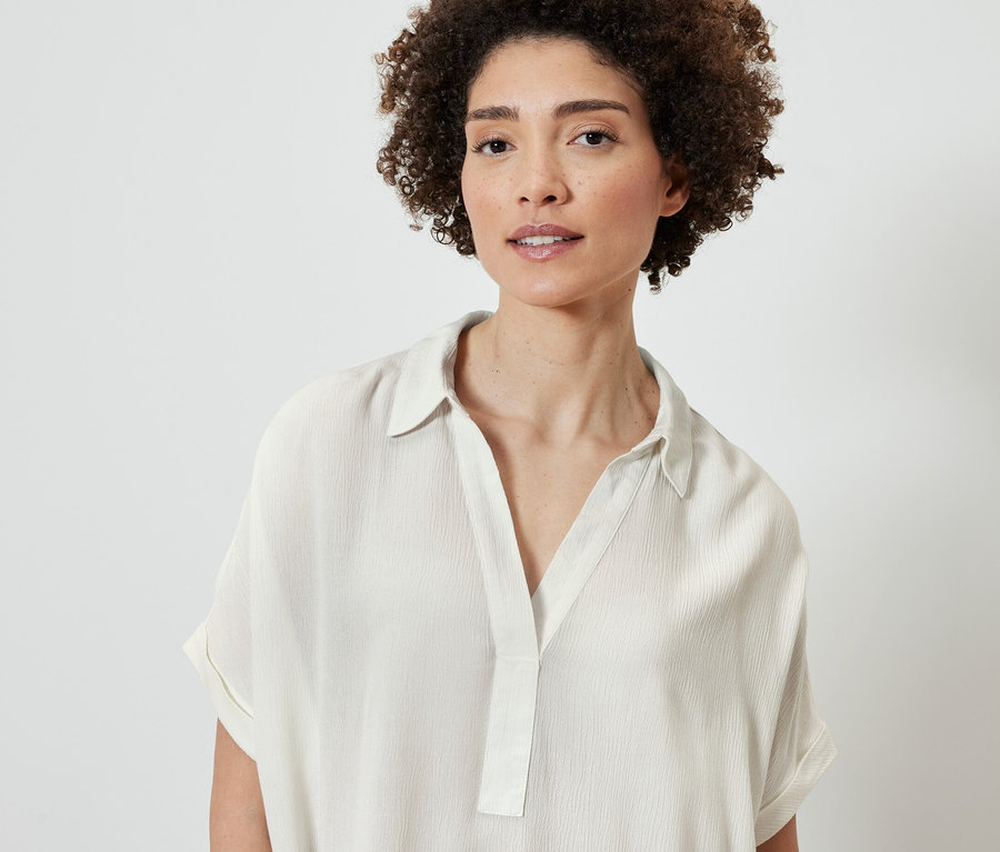 Porträt einer Frau mit braunen lockigen Haaren in einer cremeweißen Bluse.