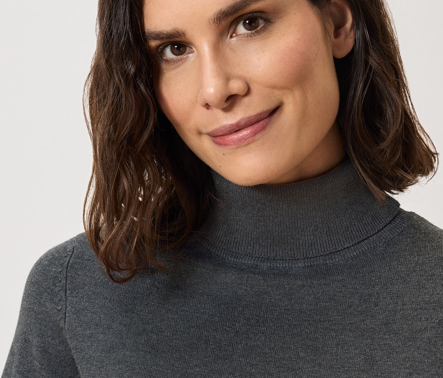 Detailaufnahme einer lächelnden Frau mit braunen Haaren in einem grauen Rollkragenpullover.