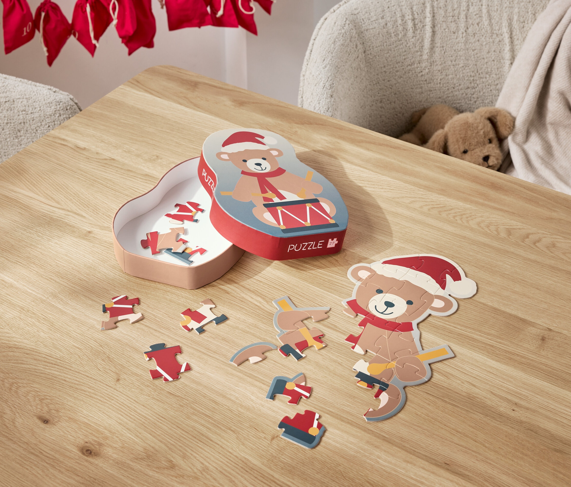 Ein Bär-Puzzle mit Weihnachtsmütze liegt zerlegt auf einem Tisch, daneben die Schachtel.