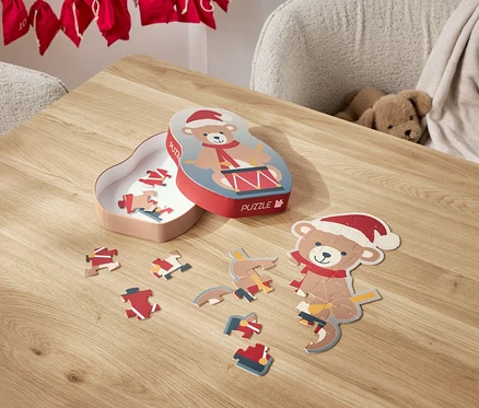 Ein Bär-Puzzle mit Weihnachtsmütze liegt zerlegt auf einem Tisch, daneben die Schachtel.