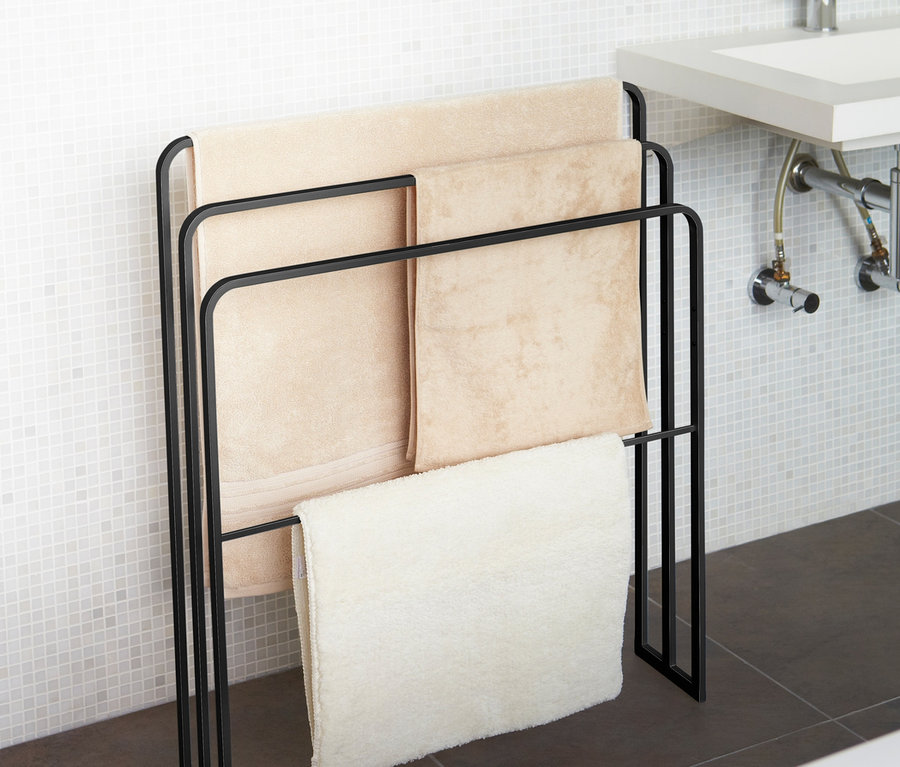 Schwarzer YAMAZAKI Badehandtuch-Ständer »TOWER« mit drei Handtüchern im Badezimmer.