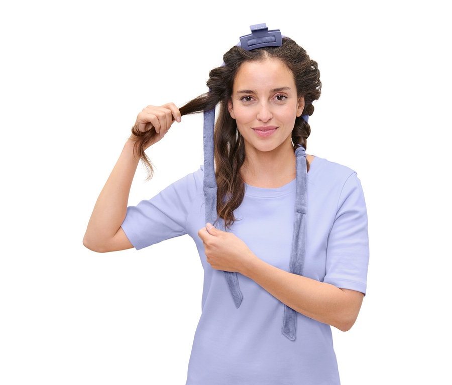 Frau wickelt ihr Haar mit einem blauen Lockenwickler.