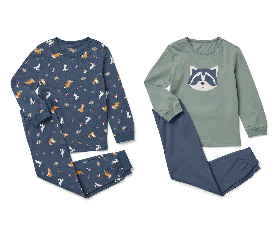 Zwei Sets Kinderpyjamas liegen nebeneinander. Ein Set ist dunkelblau mit einem Aufdruck aus Füchsen und Bäumen, das andere Set ist grün mit einem Waschbär-Aufdruck und blauen Hosen.