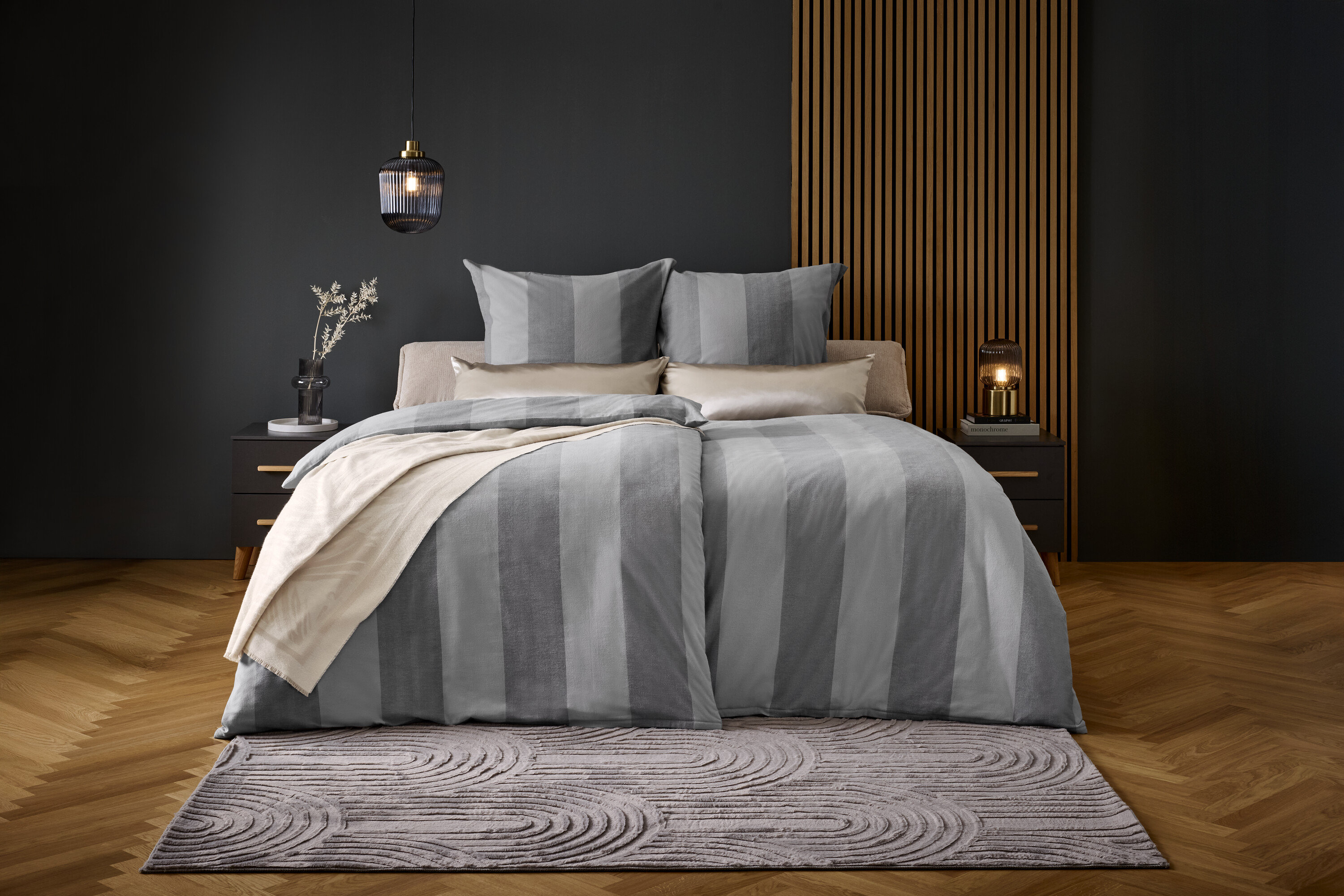 Ein Bett mit grau gestreifter Bettwäsche und Kissen auf einem grauen Teppich.