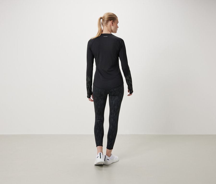 Eine Frau mit dem Rücken zur Kamera trägt ein schwarzes Langarmshirt und gemusterte Leggings.