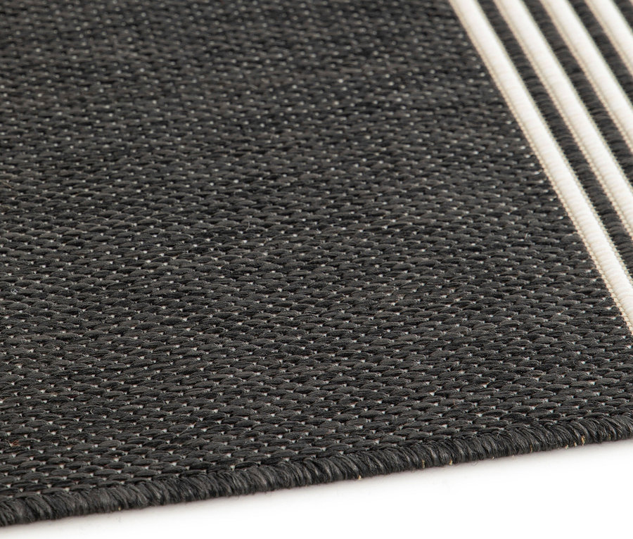 Detailansicht eines Outdoor-Teppichs »Zen Lines« mit schwarzem Hintergrund und drei weißen Streifen.